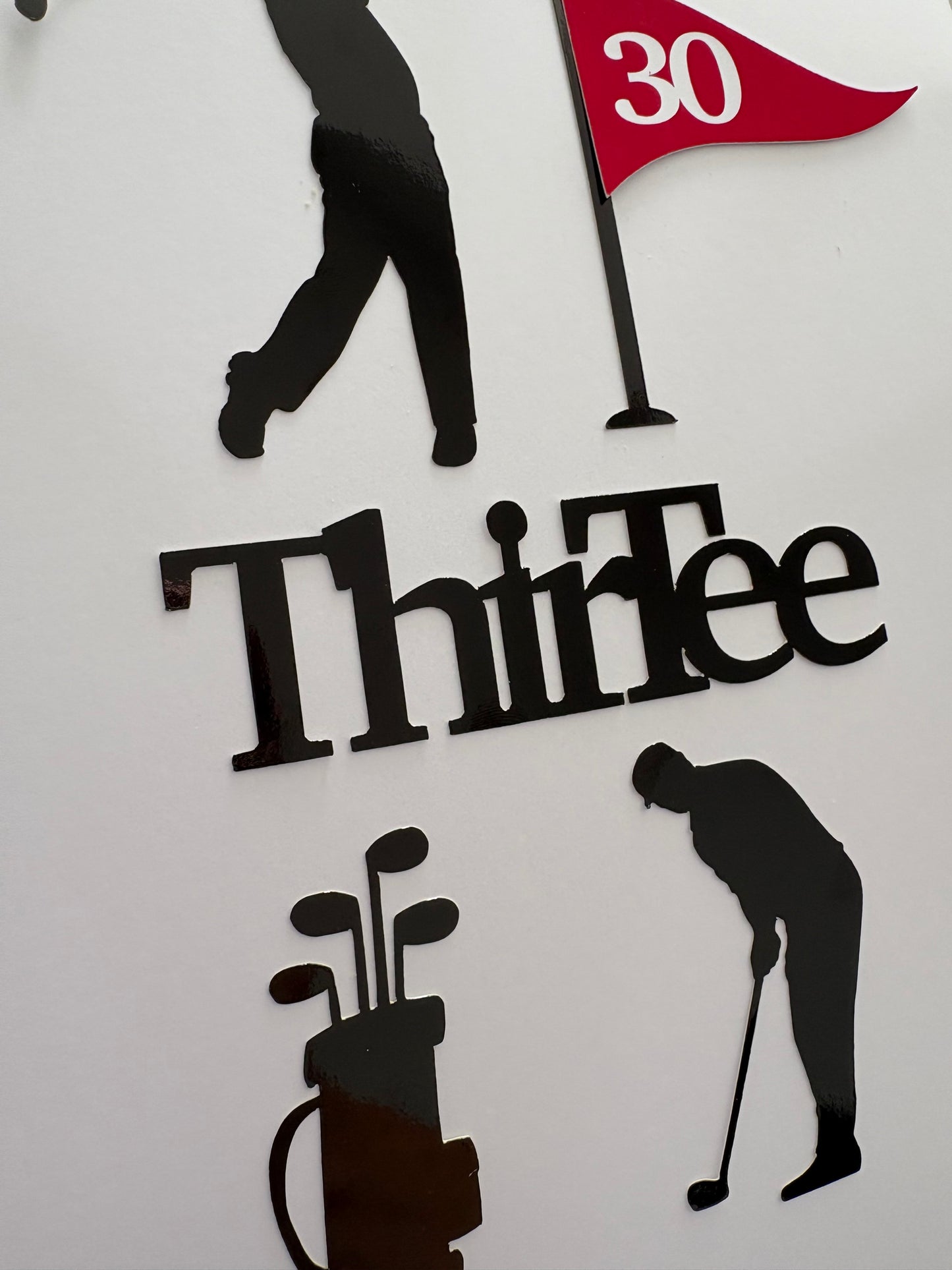 Golf-themed wall decor featuring black silhouette cutouts of golfers, a golf bag, a flag with the number 30, and the word 'ThirTee' in black lettering on a white background.