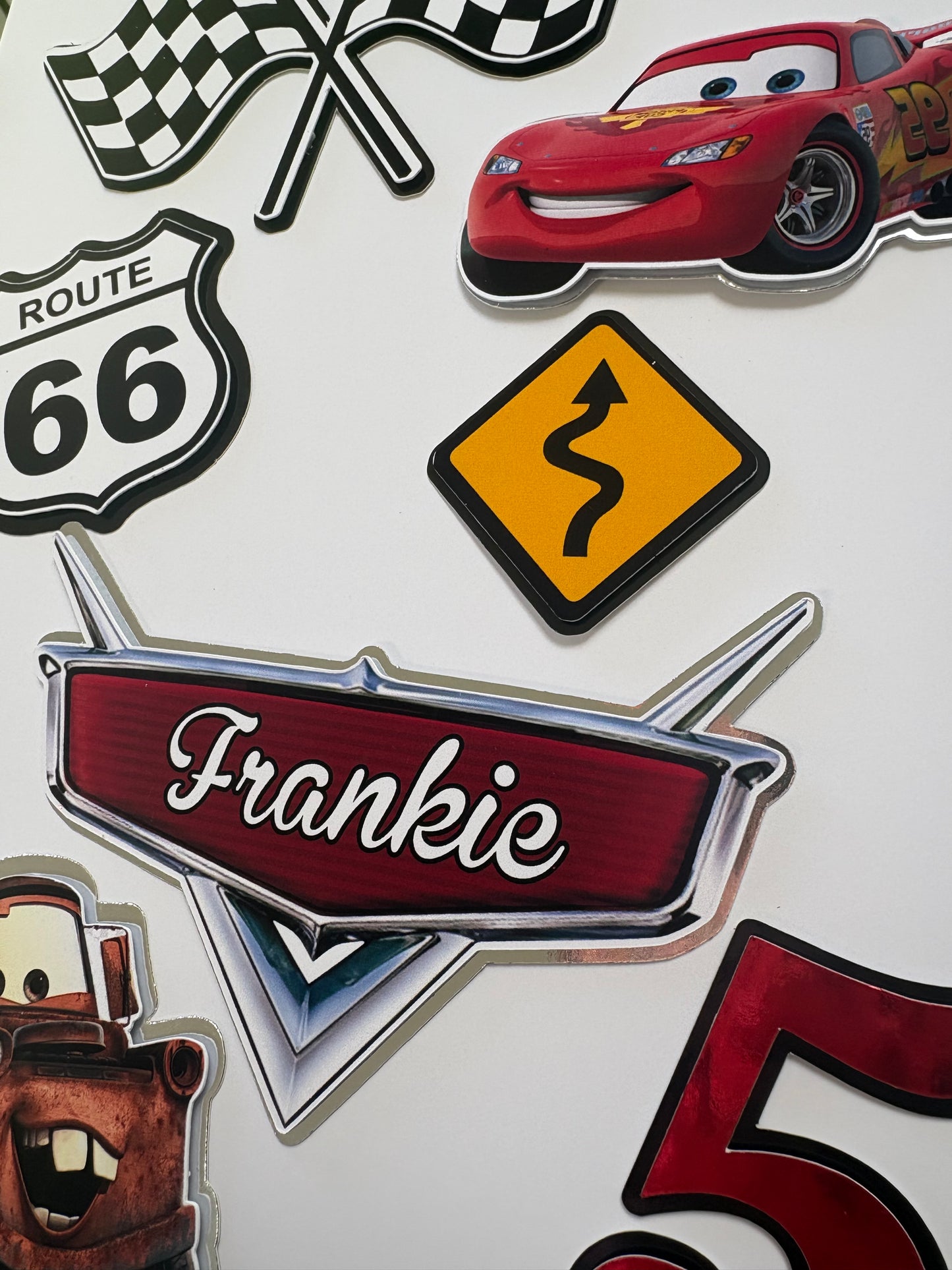 A collection of die-cut stickers featuring characters and motifs from the Disney Pixar Cars movie, displayed on a white background. The stickers include Lightning McQueen, Mater, Sally, a road sign, a checkered flag, and a sign reading 'Frankie' in script.