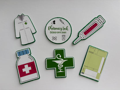 Six die-cut paper craft templates or stickers featuring pharmacy and medical designs, including a white lab coat, a circular 'Pharmacy Tech' badge, a syringe, a medicine bottle, a green cross with a snake and staff of Asclepius, and a prescription pad, arranged on a light gray background.